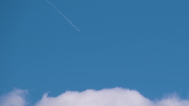 Pesawat jet penumpang yang jauh terbang di ketinggian tinggi di langit biru dengan awan putih meninggalkan jejak asap kontrail di belakang. Konsep perjalanan udara — Stok Video