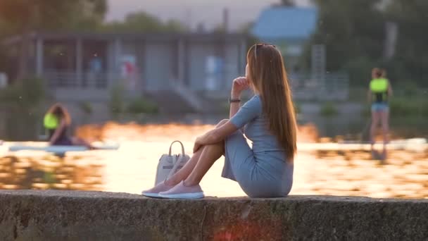 Vista lateral da mulher solitária sentada sozinha na margem do lago na noite quente. Solidão e relaxamento no conceito de natureza — Vídeo de Stock