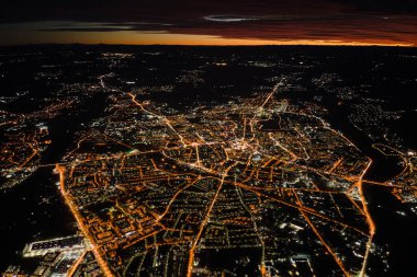 Uçak penceresinden gökyüzü manzarası ve şehrin yerleşim alanındaki aydınlık sokaklar. Yüksek irtifada karanlık şehir manzarası