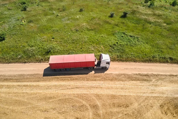 Вид с воздуха на грузовой грузовик, движущийся по грунтовой дороге между сельскохозяйственными пшеничными полями. Перевозка зерна после уборки комбайном во время уборочного сезона — стоковое фото