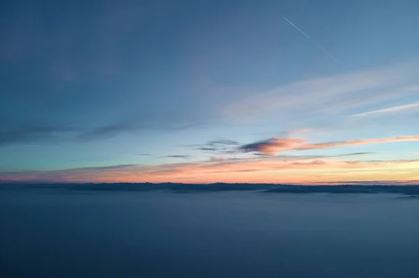 Vista aérea de colorido atardecer sobre nubes de niebla blanca densa cubierta con siluetas oscuras distantes de colinas de montaña en el horizonte —  Fotos de Stock