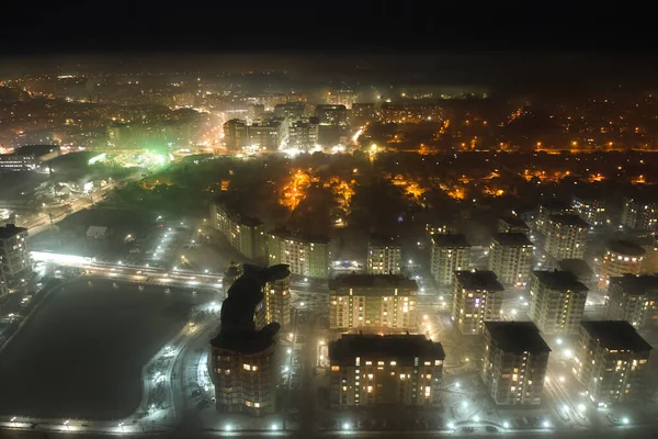 Widok z lotu ptaka wysokie budynki mieszkalne i jasne oświetlone ulice w dzielnicy mieszkalnej miasta w nocy. Ciemny krajobraz miejski — Zdjęcie stockowe