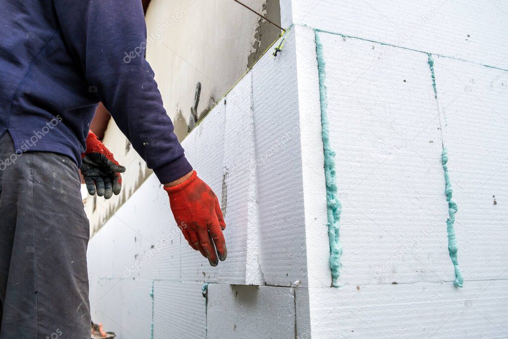Construction worker installing styrofoam insulation sheets on house facade wall for thermal protection