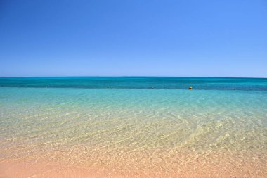Mavi deniz suyunun yüzeyi ve küçük dalgalı dalgaların sarı kumsala çarptığı deniz burnu. Seyahat ve tatil kavramı