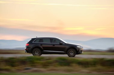 Gün batımında şehirlerarası yolda hızla giden bir SUV arabası. Akşamları otoyol trafiği