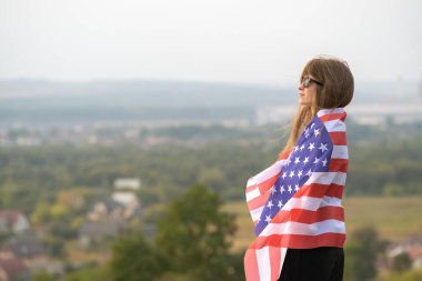 Uzun saçlı, uzun saçlı genç bir kadın rüzgârda sallanıyor. Amerikan ulusal bayrağı üzerinde, dışarıda dinleniyor. Sıcak yaz gününün tadını çıkarıyor.