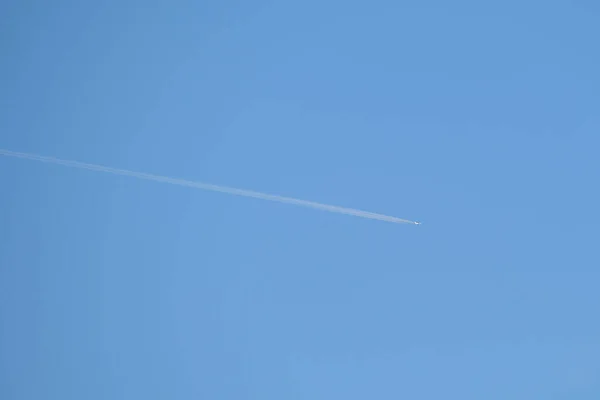 Vzdálené letadlo osobního tryskáče letí ve vysoké nadmořské výšce na jasně modré obloze a zanechává za sebou stopy bílého kouře. Koncept letecké dopravy — Stock fotografie