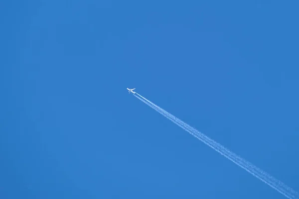 Avião de passageiros distantes voando em alta altitude no céu azul claro deixando vestígios de fumaça branca de contrail para trás. Conceito de transporte aéreo — Fotografia de Stock