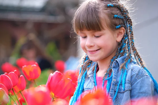 Glad barn flicka njuter söt lukt av röda tulpan blommor i sommar trädgård — Stockfoto