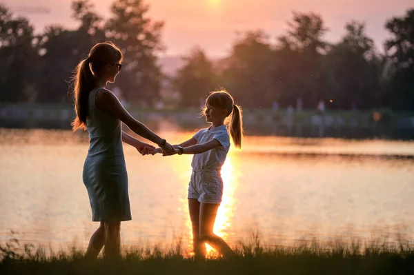 Happy mother and daughter standing together holding hands enjoying time in summer park in evening. Family love and relationship concept — Stock Photo, Image
