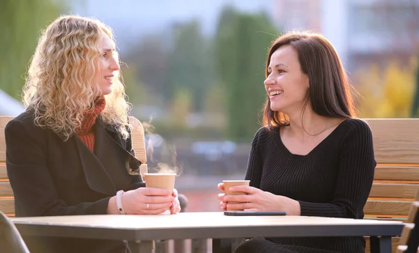 Two happy young women sitting at city street cafe havinh fun time together during coffee break