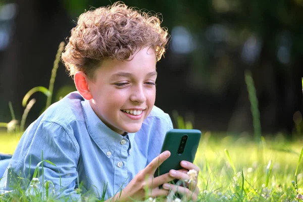 Niño jugando juego en su teléfono inteligente al aire libre en el parque de verano. Adicción desde el concepto de aparatos electrónicos — Foto de Stock