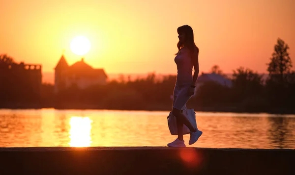 평상복 차림의 젊은 여자가 따뜻 한 저녁에 호수 옆을 걷고 있다. 여름 방학 과 여행의 개념 — 스톡 사진