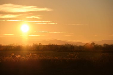 Güzel bir akşam panoramik manzarası. Gün batımında güneş batarken uzak dağ tepeleri ve asfalt yolda batıyor.