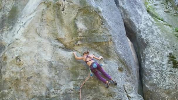 Odhodlaná horolezkyně šplhá po příkré stěně skalnaté hory. Sportovkyně překonává obtížnou cestu. Zapojení do extrémních sportů a horolezectví hobby koncept — Stock video