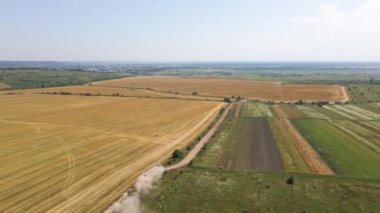 Tarım buğday tarlaları arasında toprak yolda giden kargo kamyonunun hava görüntüsü çok toz yapıyor. Hasat mevsiminde hasatçıların topladığı tahıl naklinden sonra.