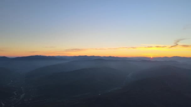 Luftaufnahme dunkler Berghügel mit hellen Sonnenstrahlen der untergehenden Sonne bei Sonnenuntergang. Dunstige Gipfel und neblige Täler am Abend — Stockvideo