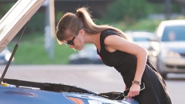 Ανήμπορη γυναίκα στέκεται κοντά στο αυτοκίνητό της με ανοιχτή κουκούλα takling στο κινητό τηλέφωνο καλώντας την οδική υπηρεσία για βοήθεια. Νεαρή γυναίκα οδηγός που έχει πρόβλημα με το όχημα — Αρχείο Βίντεο