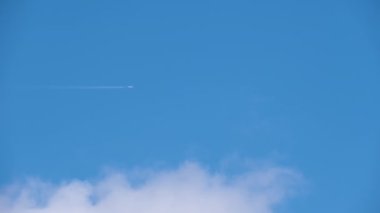 Uzaktaki yolcu uçağı mavi gökyüzünde yüksek irtifada uçarken beyaz bulutlar ardında iz bırakıyor. Hava yolculuğu konsepti