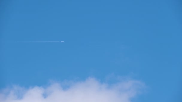 Avionul de pasageri îndepărtat care zboară la mare altitudine pe cerul albastru, cu nori albi lăsând urme de fum de contrail în urmă. Conceptul de călătorie aeriană — Videoclip de stoc