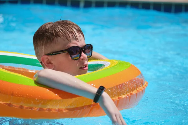 Portrait d'un enfant garçon heureux se relaxant dans un cercle gonflable dans la piscine le jour ensoleillé de l'été pendant les vacances tropicales. Concept d'activités estivales — Photo