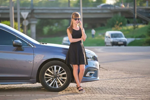 Mujer elegante conductor de pie cerca de su vehículo hablando por teléfono celular en la calle de la ciudad en verano — Foto de Stock