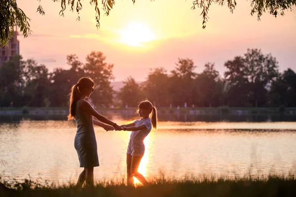 Gelukkig moeder en dochter meisje ontspannen hand in hand genieten van de tijd samen in de zomer park bij zonsondergang. Familie liefde en relatie concept — Stockfoto