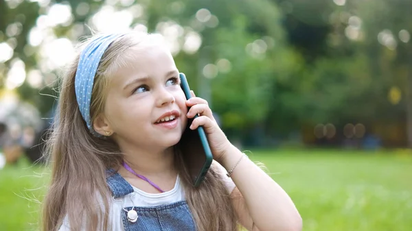 Feliz niña teniendo conversación hablando por teléfono móvil en el parque de verano — Foto de Stock