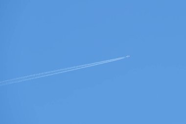 Mesafeli yolcu jet uçağı açık mavi gökyüzünde yüksek irtifada uçarken ardında beyaz duman izi bırakıyor. Hava taşımacılığı kavramı
