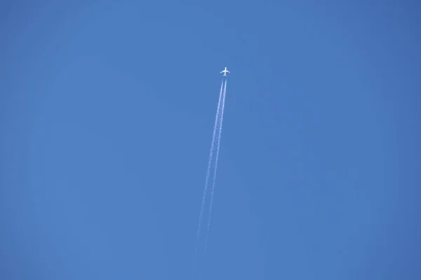 Avião de passageiros distantes voando em alta altitude no céu azul claro deixando vestígios de fumaça branca de contrail para trás. Conceito de transporte aéreo — Fotografia de Stock