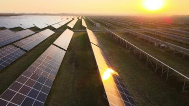 Günbatımında temiz elektrik enerjisi üretmek için birçok sıra güneş fotovoltaik paneli bulunan sürdürülebilir büyük elektrik santralinin havadan görünüşü. Sıfır emisyon kavramı ile yenilenebilir elektrik