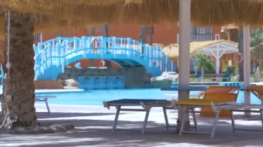 Boş güverte sandalyeleri, tropik tatil köylerinde havuz kenarında saman gölgesi şemsiyelerinin altında. Yaz tatilleri ve kaçış konsepti