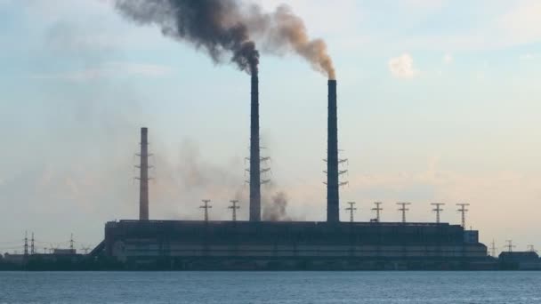 Kol kraftverk höga rör med svart rök rör sig uppåt förorenande atmosfär över sjön vatten — Stockvideo