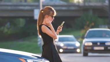 Aracının yanında duran şık kadın sürücü yazın şehir caddesinde cep telefonuyla konuşuyor.