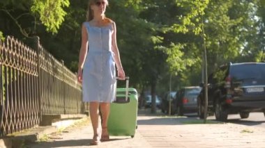Yaz günü yeşil bavulla şehir caddesinde yürüyen genç bir kadın. Seyahat ve tatil kavramı