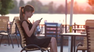 Genç bir kadın sıcak bir yaz akşamında sokak kafeteryasında cep telefonuyla konuşuyor. İletişim ve mobil bağlantı kavramı.