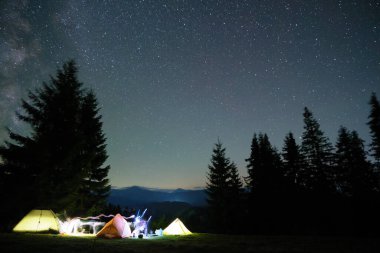 Gece yıldızlarının altındaki karanlık dağlardaki kamp alanında parlayan parlak kamp çadırları gökyüzünü kapladı. Aktif yaşam tarzı ve seyahat konsepti