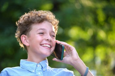 Yazlık parkta cep telefonuyla konuşan mutlu genç çocuk.