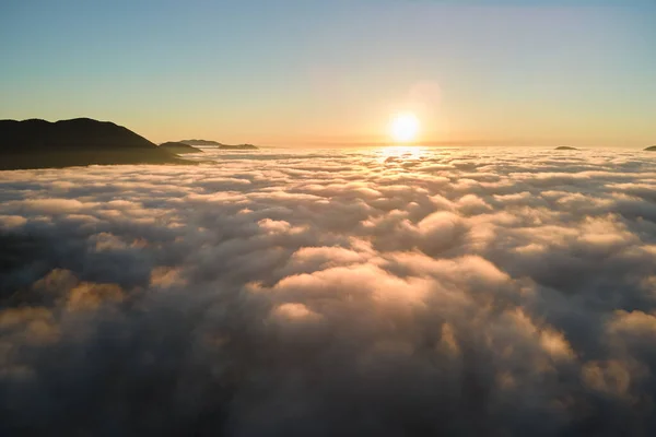 Vista aérea del colorido amanecer sobre la densa niebla blanca con siluetas oscuras distantes de colinas de montaña en el horizonte —  Fotos de Stock