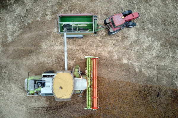 Aerial view of combine harvester unloading grain in cargo trailer working during harvesting season on large ripe wheat field. Agriculture and transportation of raw farm products concept — Stock Photo, Image