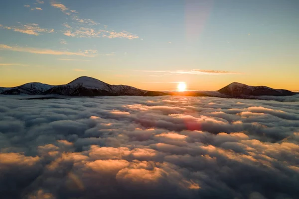 Vista aérea del vibrante amanecer sobre densas nubes blancas con lejanas montañas oscuras en el horizonte — Foto de Stock