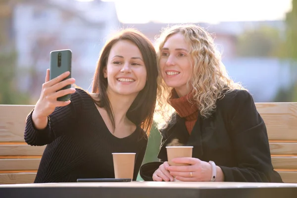 Namoradas alegres tomando selfie com sellphone descansando no café da rua da cidade. Amigos do sexo feminino curtindo o tempo juntos ao ar livre no dia quente — Fotografia de Stock