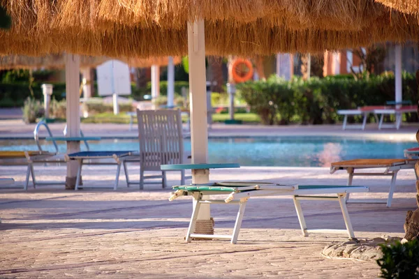열 대 휴양지 수영장에 있는 짚 그늘 아래빈 갑판 의자들이 있다. 여름 방학 과 휴가에 대한 개념 — 스톡 사진