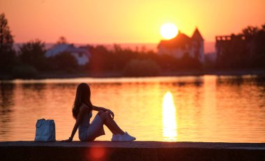 Gölün kıyısında yalnız başına oturan yalnız genç kadın sıcak akşamın tadını çıkarıyor. Doğada refah ve rahatlama kavramı