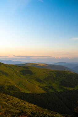 Yüksek dağların tepelerinde puslu bir akşam ve gün batımında uzak bir vadi. Alacakaranlıktaki yamaçların muhteşem manzarası