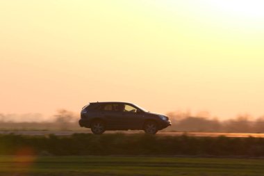 Gün batımında şehirlerarası yolda hızla giden bir SUV arabası. Akşamları otoyol trafiği