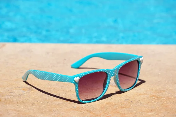 Крупним планом блакитні сонцезахисні окуляри на стороні басейну в теплий сонячний день. Концепція літніх канікул — стокове фото