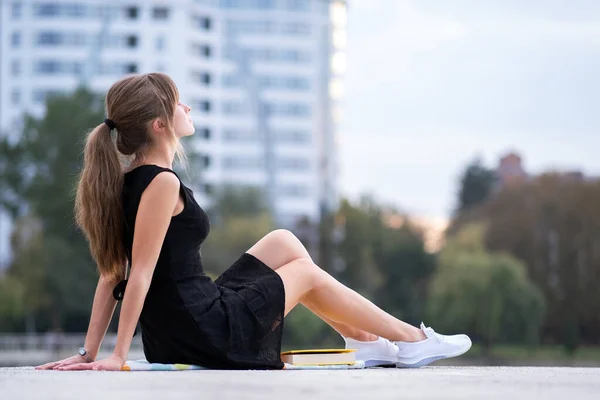 Молодая женщина, сидящая одна на городской улице, наслаждается теплым летним днем. Здоровье и отдых на свежем воздухе — стоковое фото