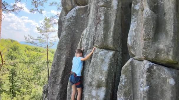 Odhodlaný horolezec šplhá po příkré stěně skalnaté hory. Dítě překonává obtížnou cestu. Zapojení do extrémních sportů a horolezectví hobby koncept — Stock video