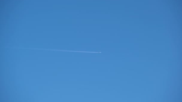 Distant passenger jet plane flying on high altitude on clear blue sky leaving white smoke trace of contrail behind. Air transportation concept — Stock Video